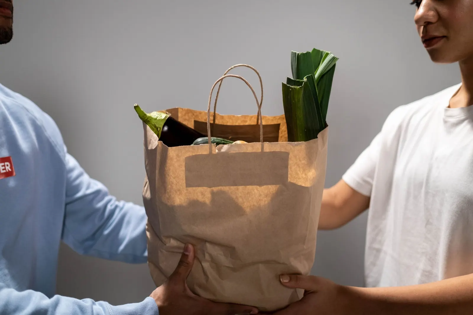 Deux personnes se passent un sac en papier contenant des légumes, lors d'une distribution d'aide alimentaire