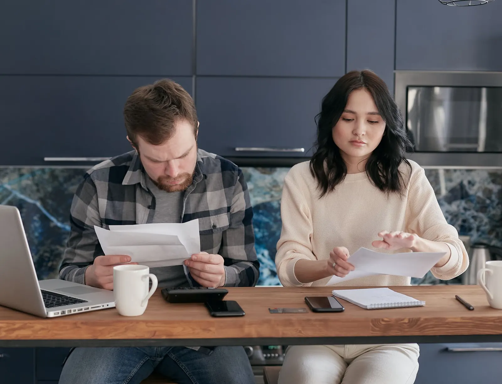 Un couple examine des factures et des courriers à la table de la cuisine, l'air préoccupé