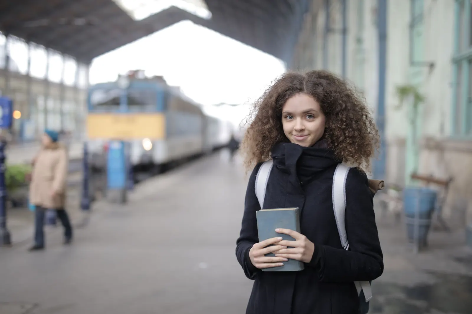Jeune femme avec un sac à dos et un livre sur le quai d'une gare, un train à l'arrêt derrière elle