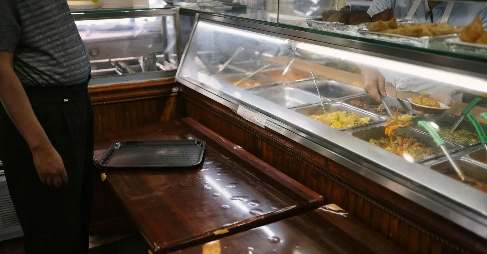 Plateau posé devant un comptoir de restauration collective où sont présentés des plats chauds