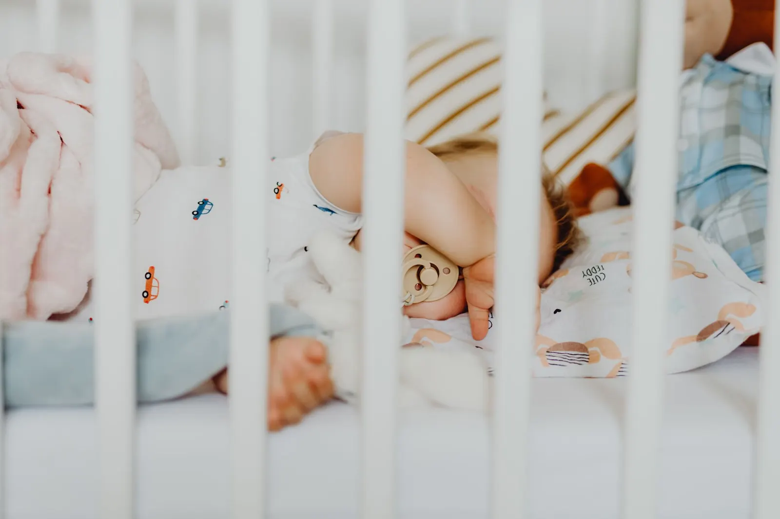 Gros plan sur un bébé endormi dans un lit à barreaux, entouré de peluches et de couvertures