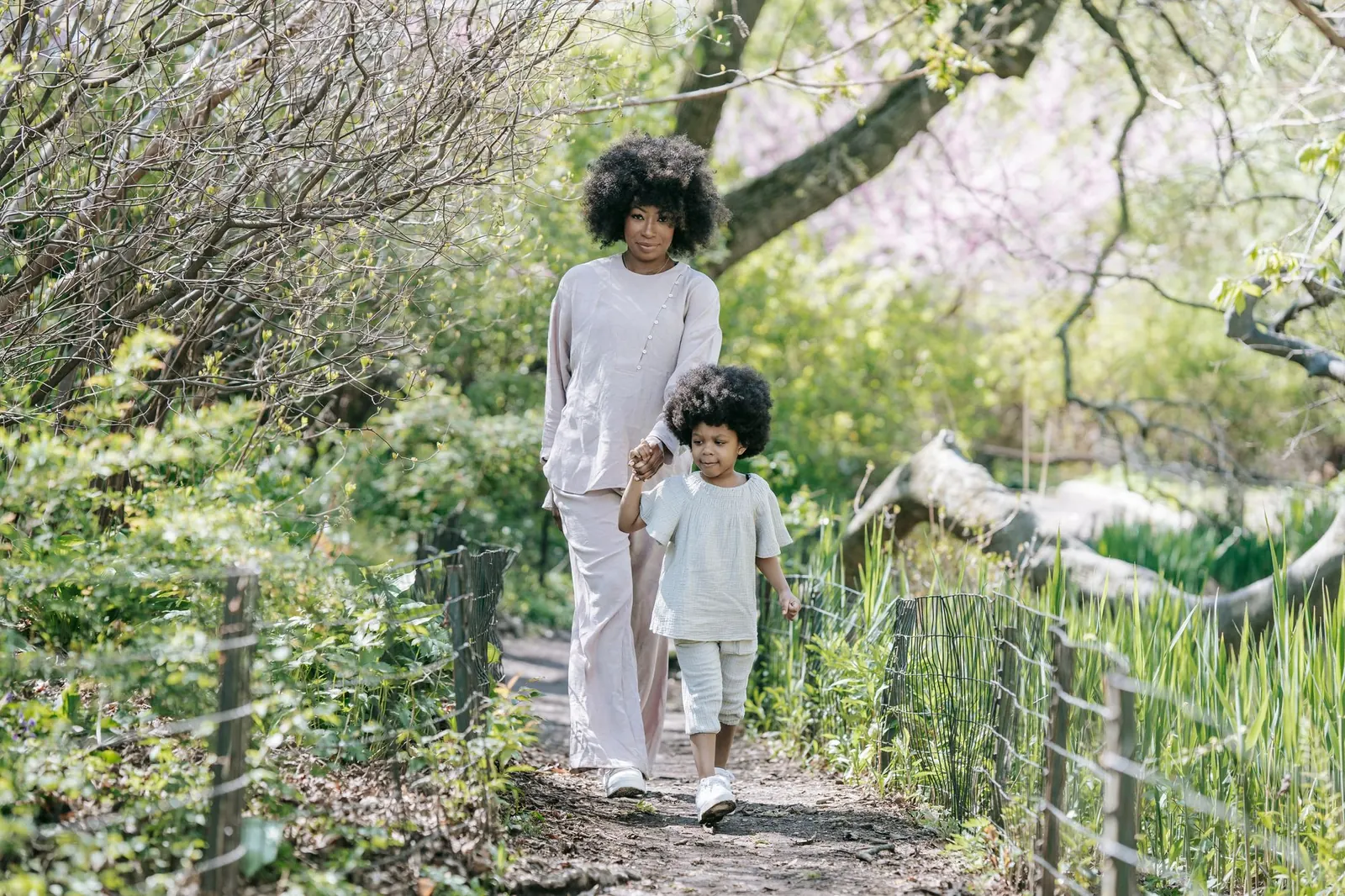 Une mère et sa petite fille marchent main dans la main sur un chemin de parc au printemps