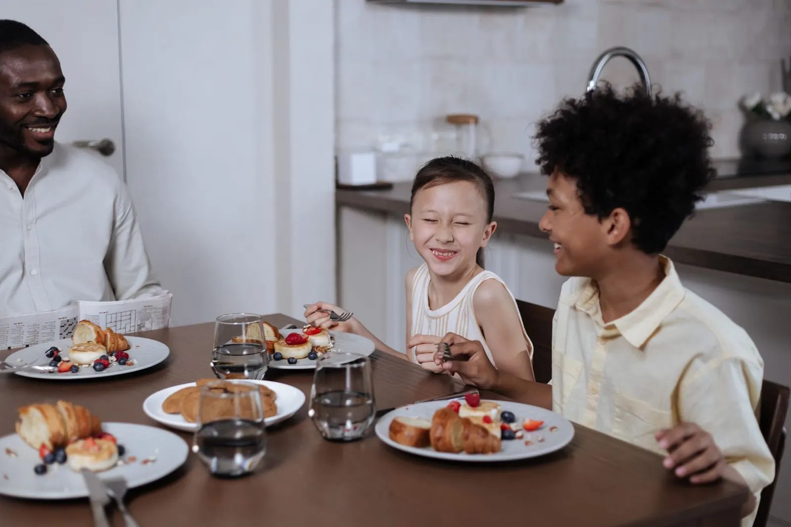 Un père et deux enfants rient en prenant un petit-déjeuner autour d'une table de cuisine