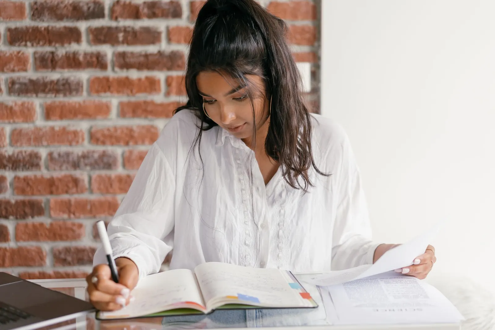 Jeune femme prenant des notes dans un cahier, des documents posés devant elle