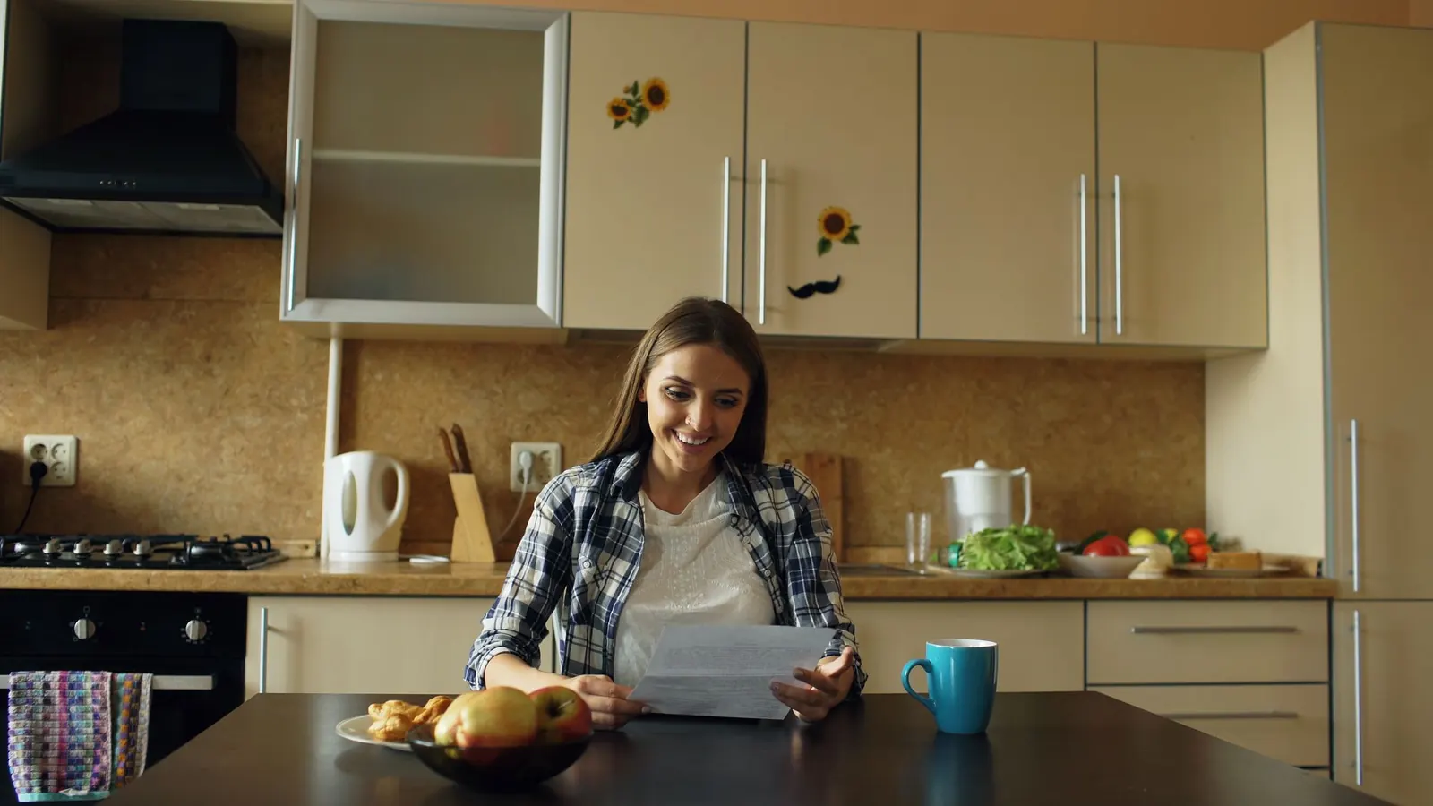 Jeune femme souriante lisant un courrier à la table d'une cuisine