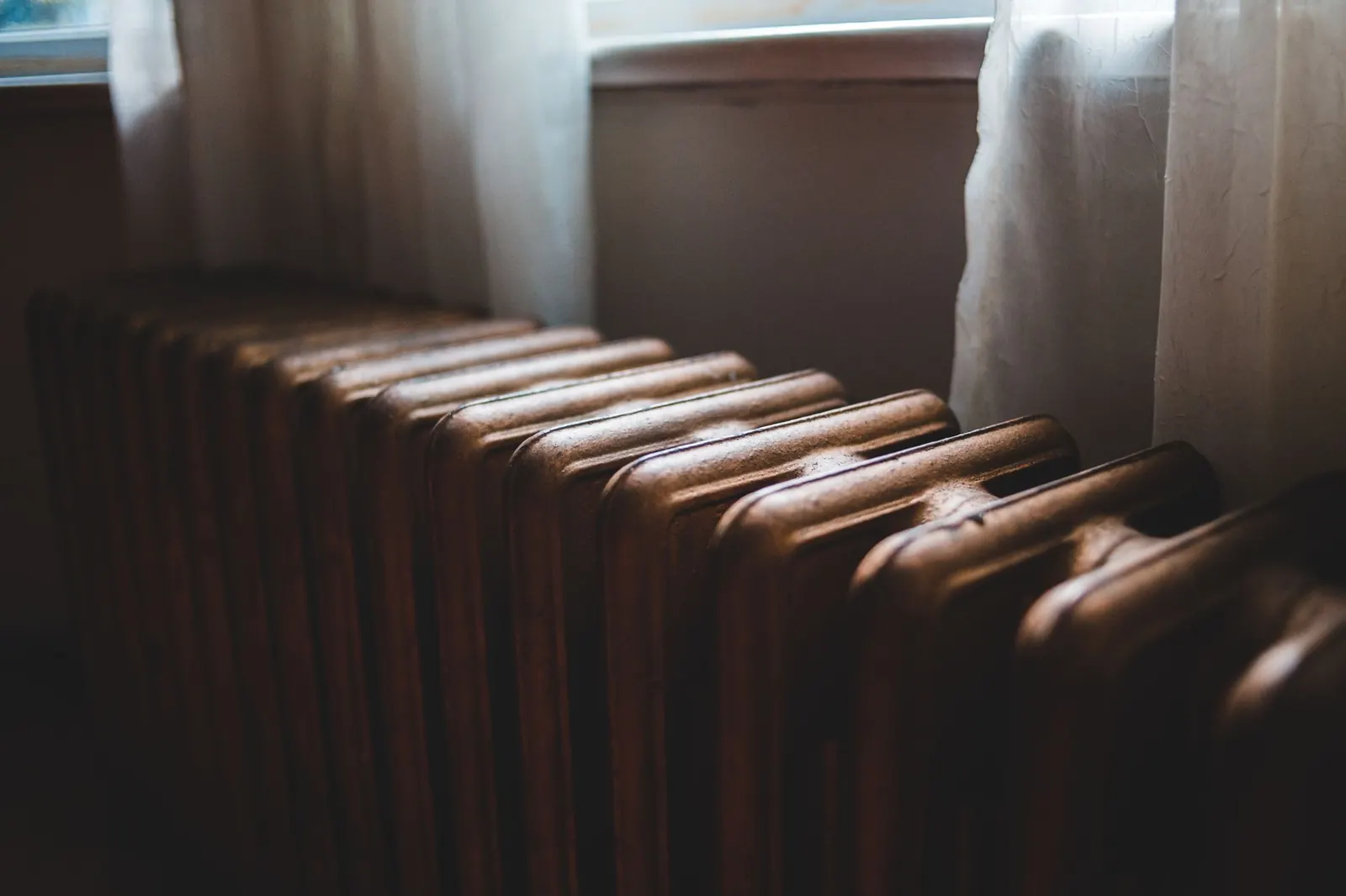 Radiateur en fonte à côté d'une fenêtre aux rideaux clairs, dans un logement