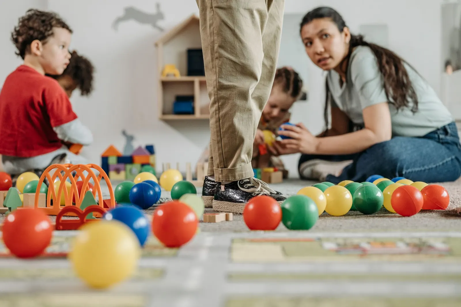 Une professionnelle de la petite enfance assise par terre joue avec des enfants dans une salle remplie de balles colorées et de jouets