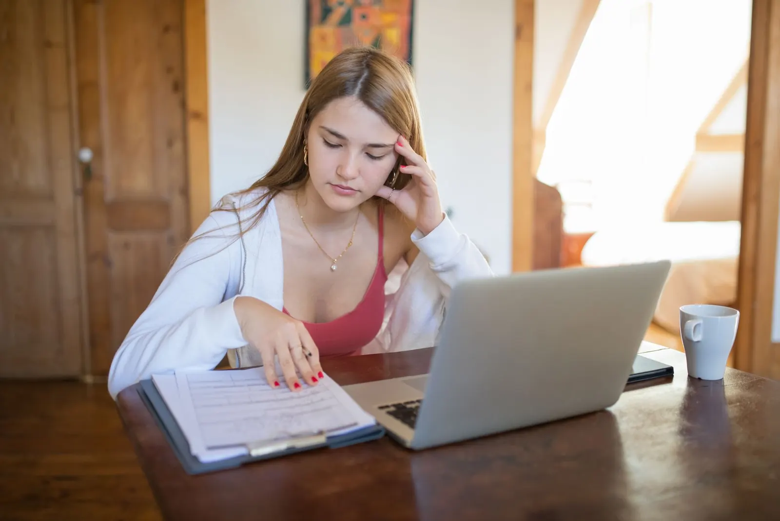 Jeune femme penchée sur des documents devant un ordinateur portable, une tasse posée sur la table