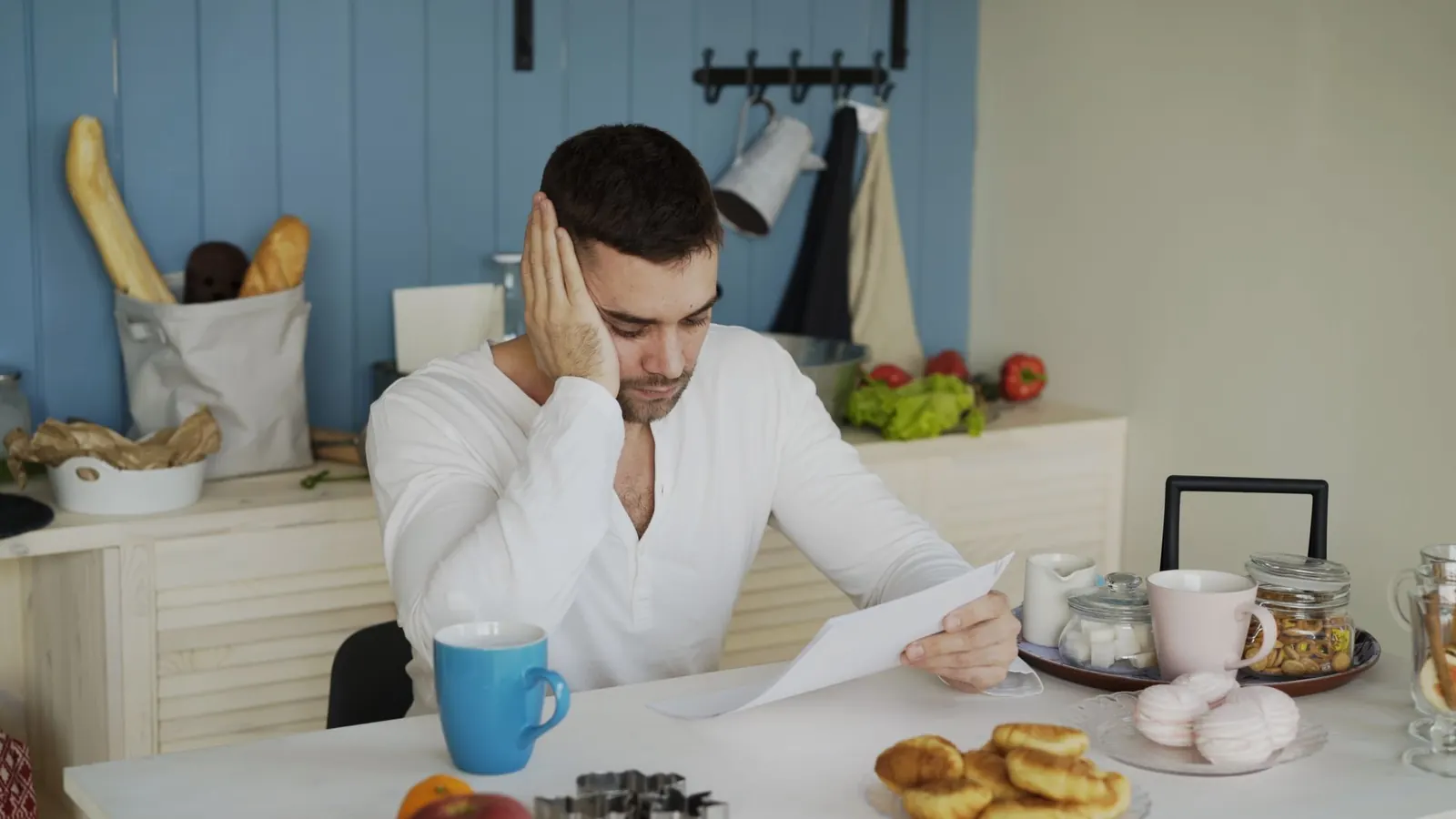 Homme qui lit un courrier assis à une table de cuisine devant un petit-déjeuner