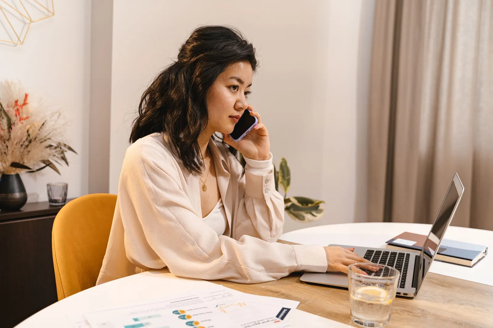 Femme au téléphone devant un ordinateur portable, des documents posés sur la table