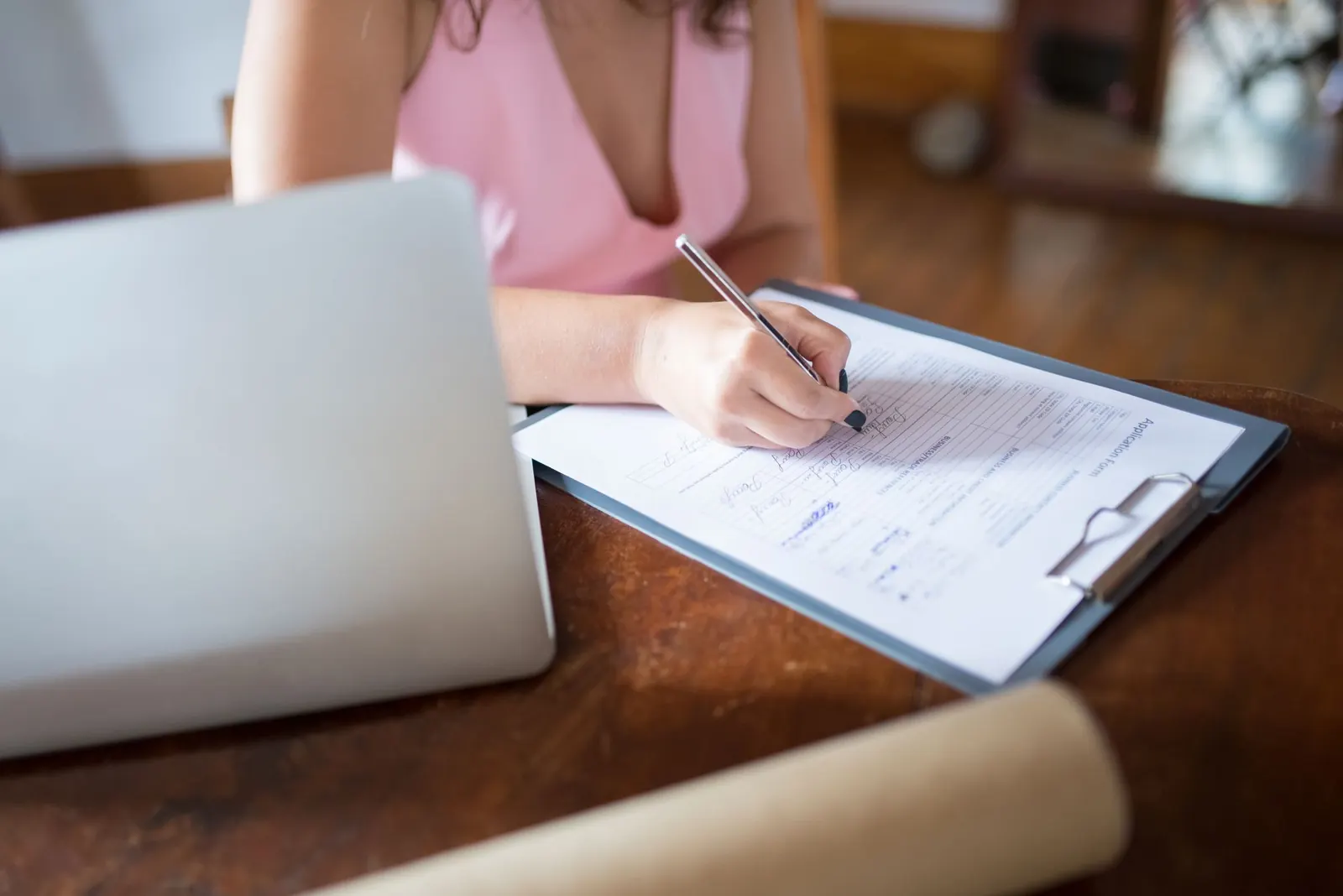 Femme remplissant un formulaire papier sur un support à pince, un ordinateur portable à côté