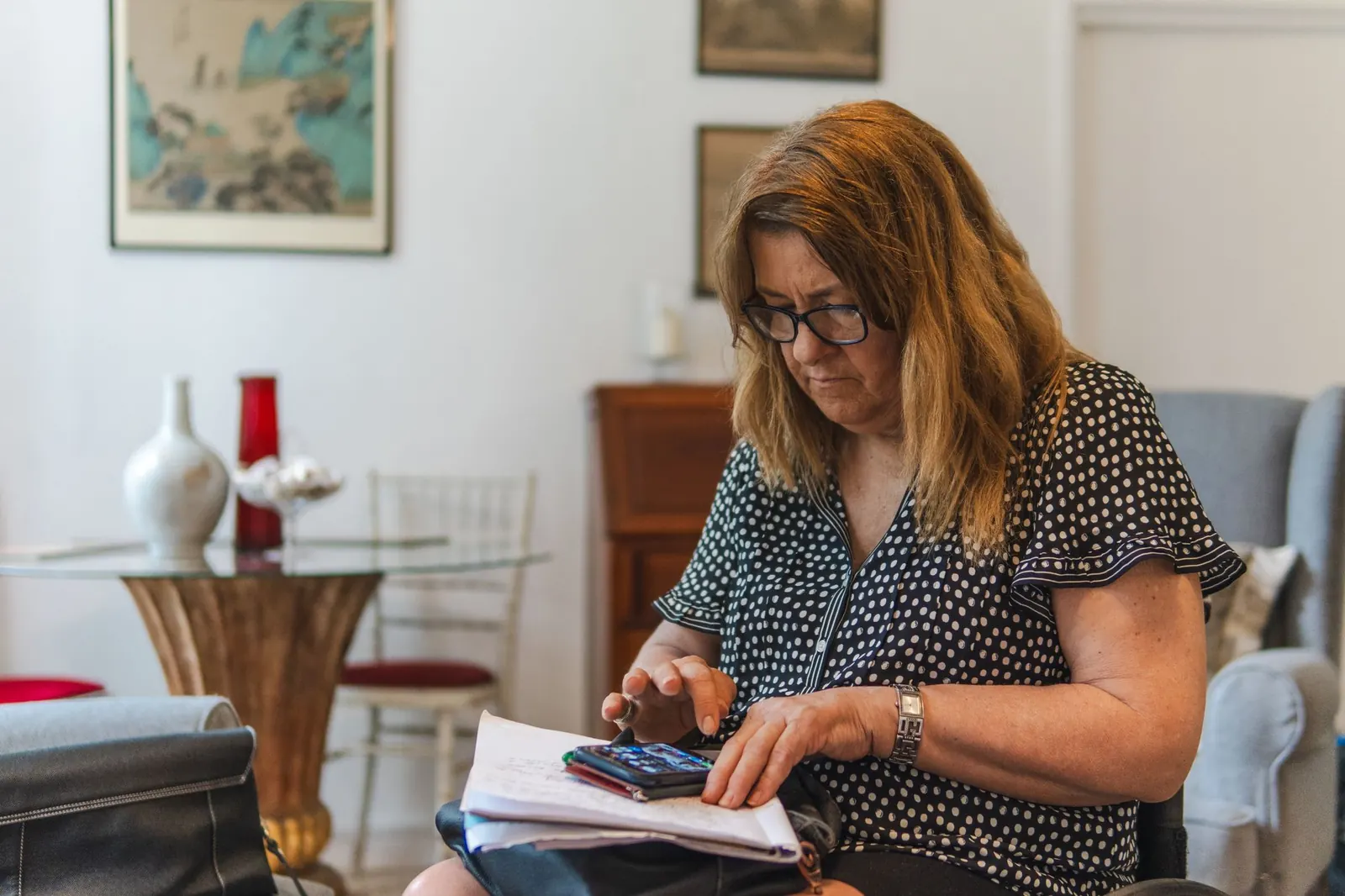 Femme assise sur un canapé qui fait un calcul avec une calculatrice et un carnet de comptes
