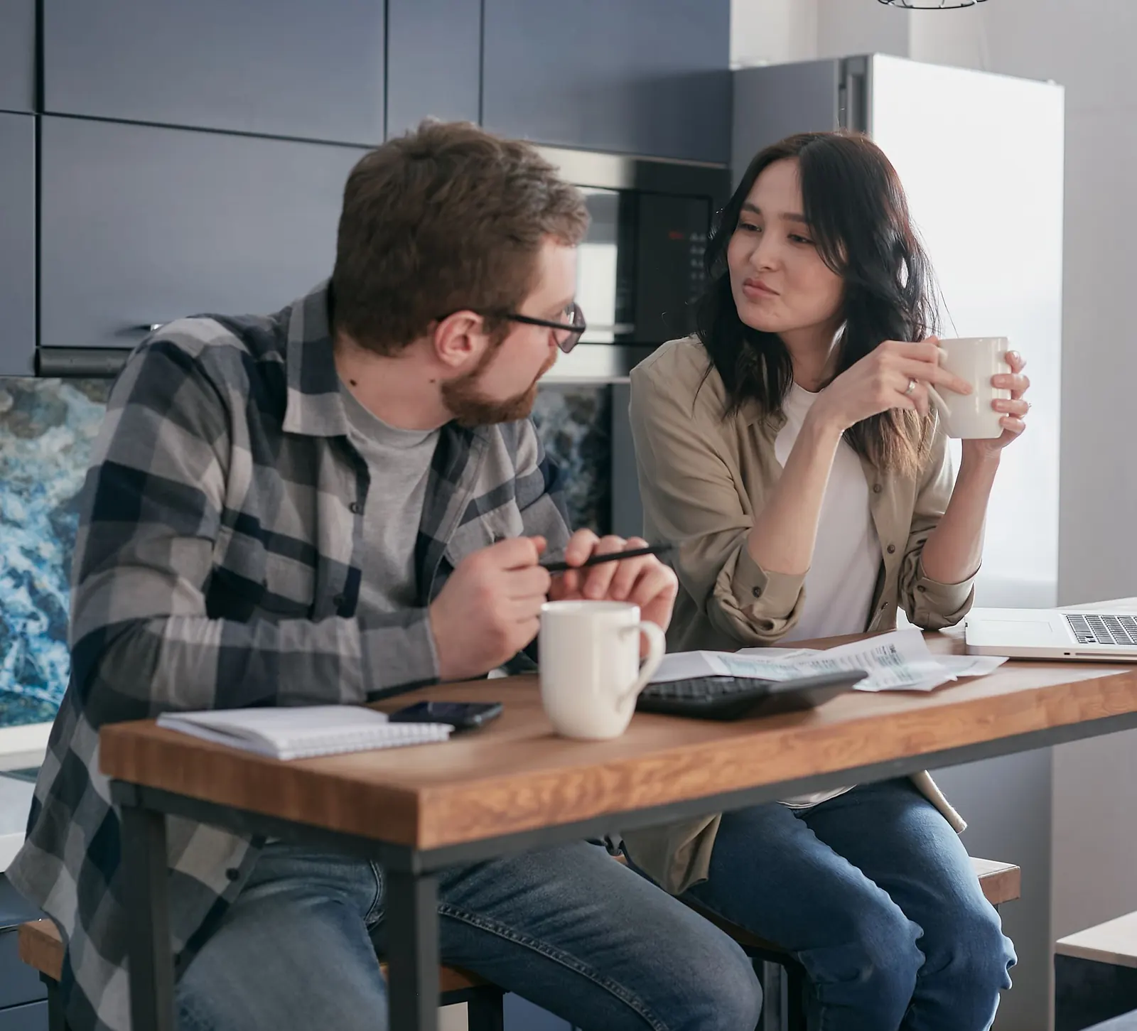 Un couple discute autour d'une table de cuisine avec des papiers, une calculatrice et un ordinateur portable
