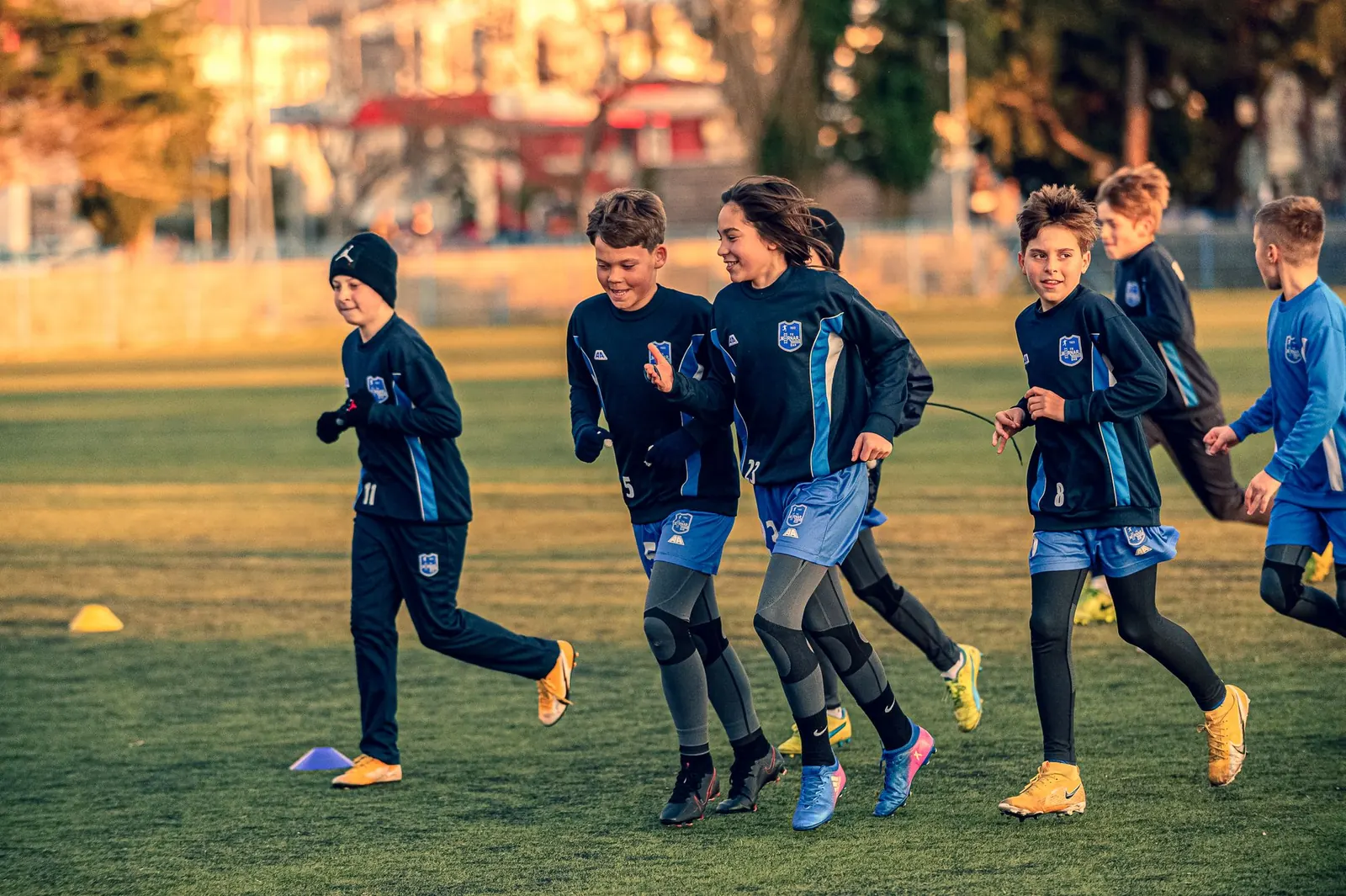 Groupe d'enfants en tenue de club qui courent ensemble sur un terrain en herbe à la tombée du jour