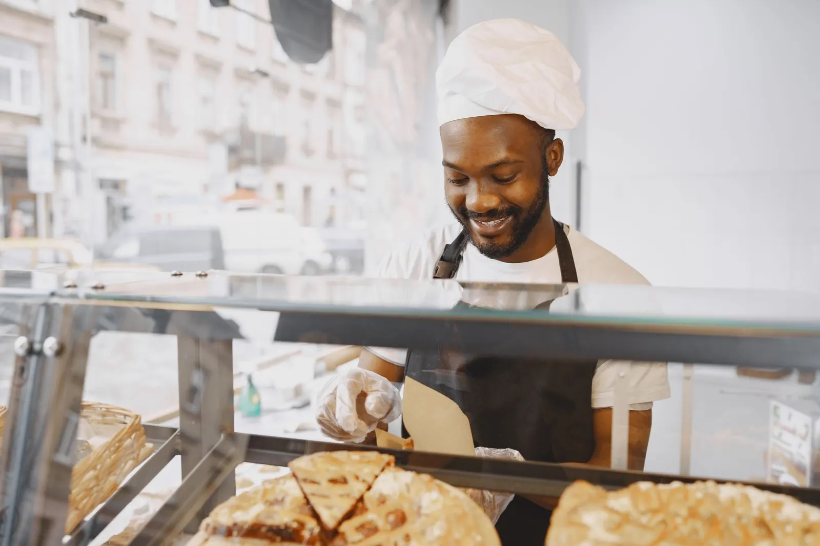 Boulanger en tablier servant des pâtisseries derrière la vitrine d'une boulangerie