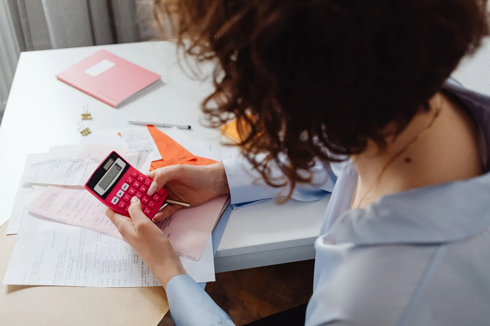 Femme qui calcule ses dépenses à son bureau, une calculatrice et des documents devant elle