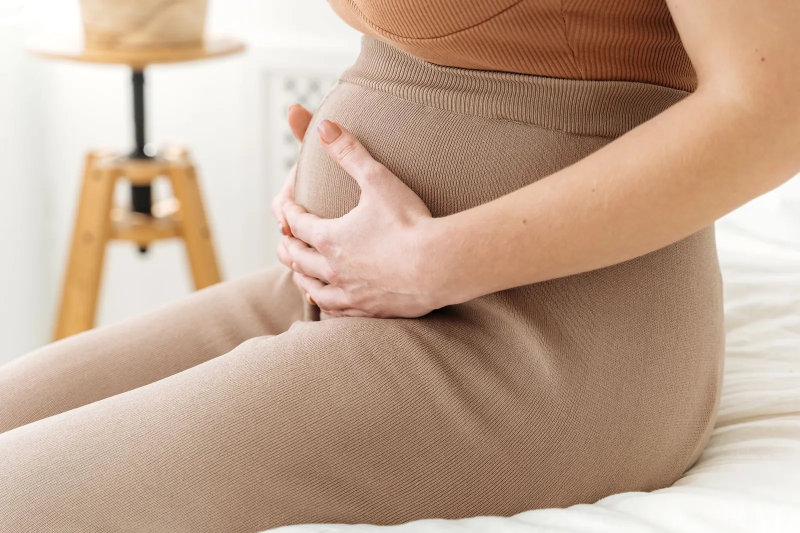 Gros plan sur une femme enceinte qui pose les mains sur son ventre, dans une lumière douce