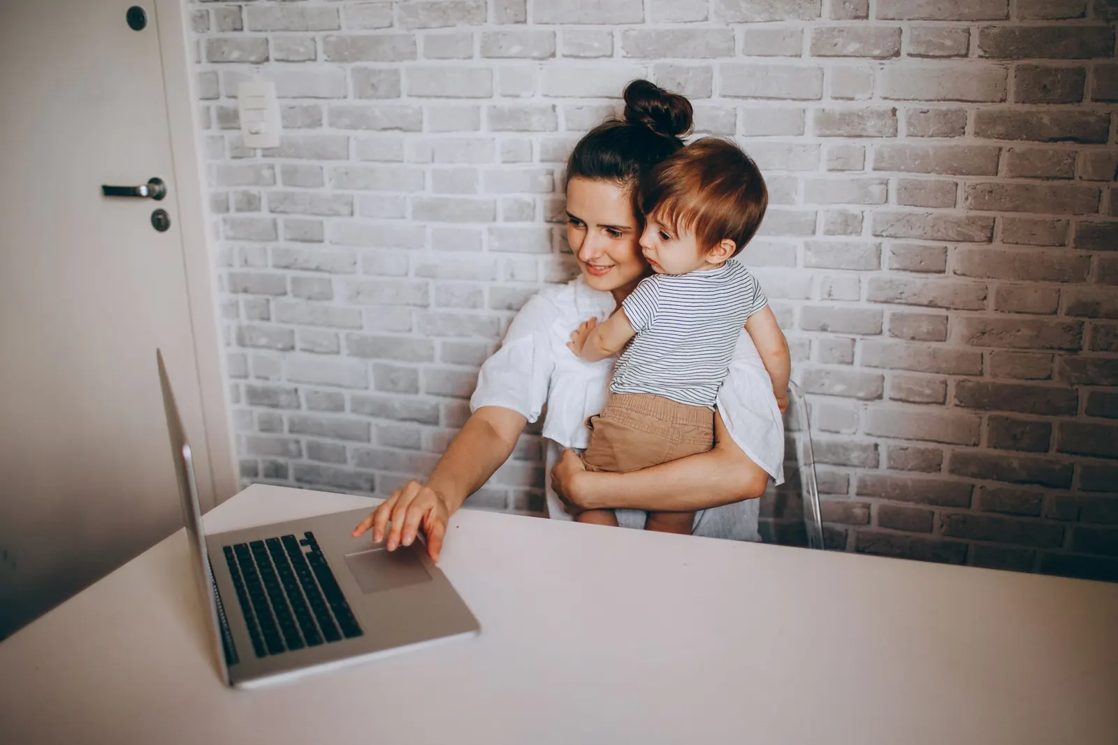 Jeune mère portant son enfant devant un ordinateur portable, assise à une table