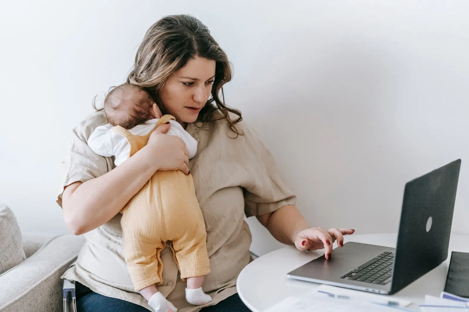 Jeune mère portant son nouveau-né tout en tapant sur un ordinateur portable